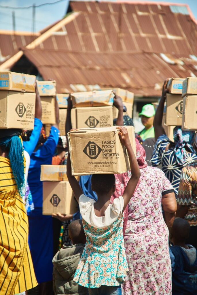 A group of people carrying boxes from Lagos Food Bank Initiative during a community support event.