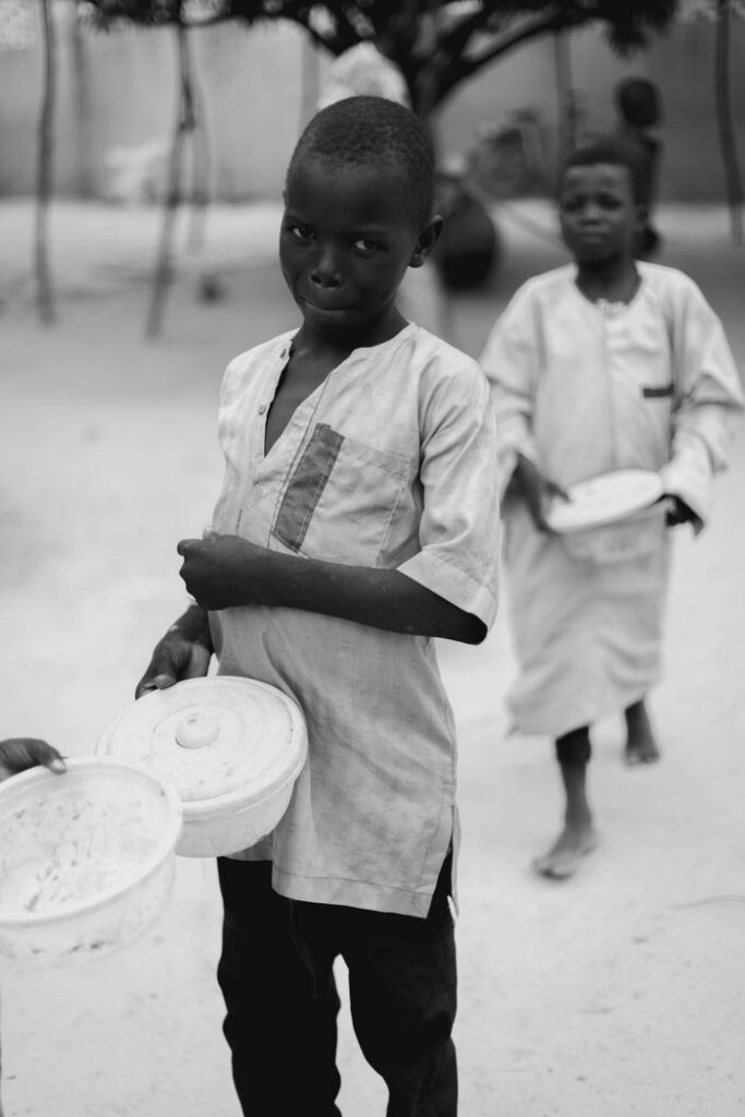 Black and white photo of children holding plates in an outdoor space, evoking thought and empathy.