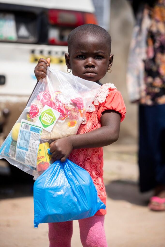 A young African girl holding relief supplies in plastic bags outdoors.
